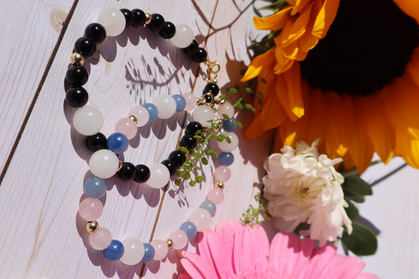 Black onyx, white moonstone and blue aventurine beaded bracelets with gold accents beside sunflowers