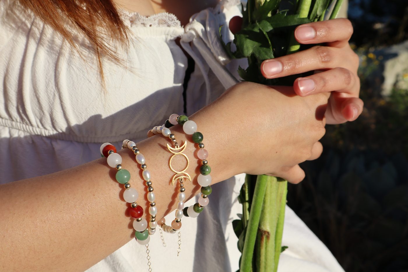 Blue angelite, rose quartz and freshwater pearl bracelets with gold beads beside sunflowers