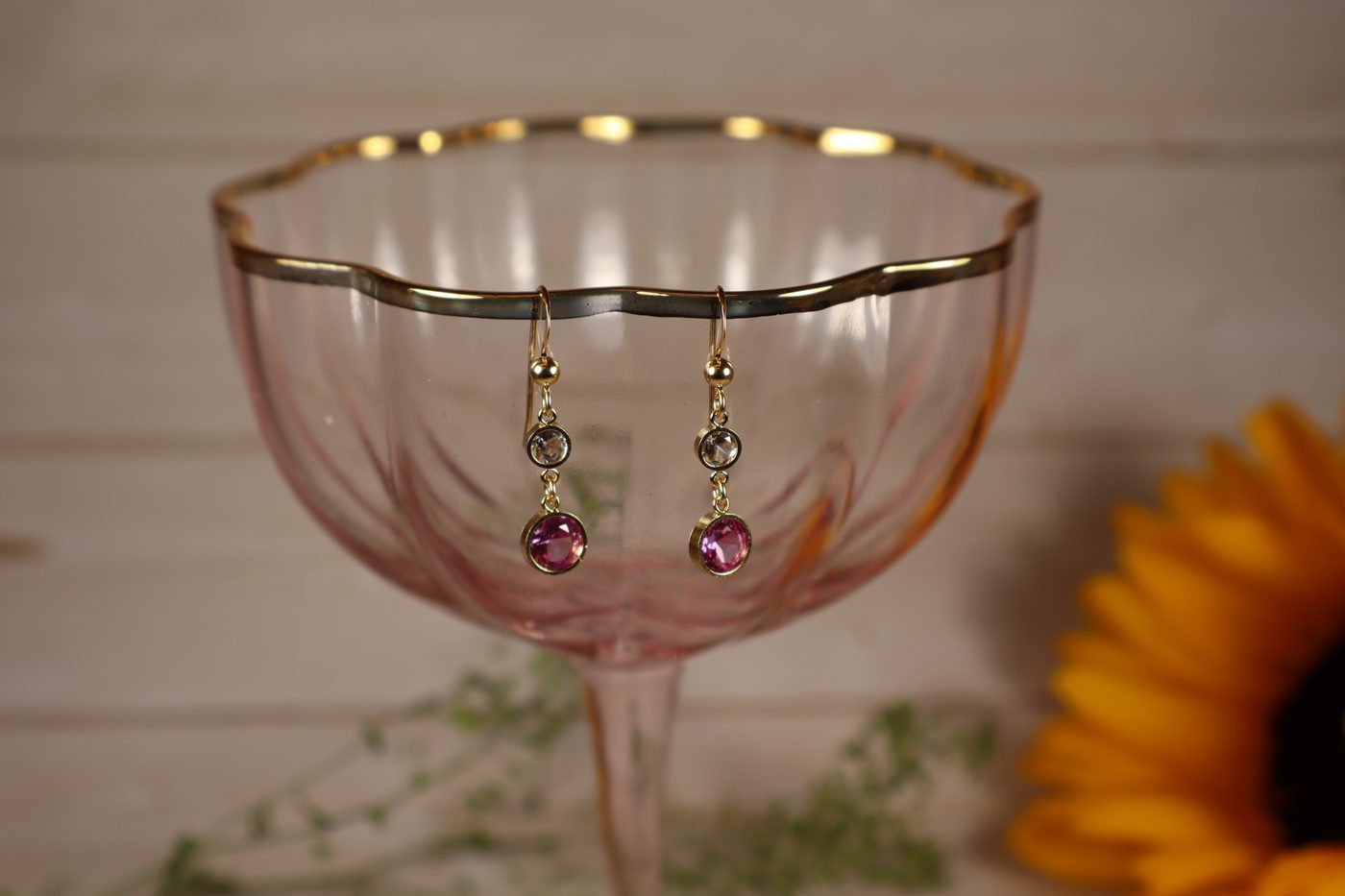 Pink sapphire and clear crystal drop earrings hanging from a vintage pink glass